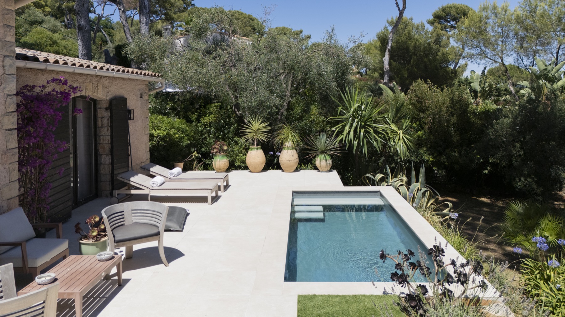 Kompakter rechteckiger Pool auf heller Terrasse mit mediterranem Garten