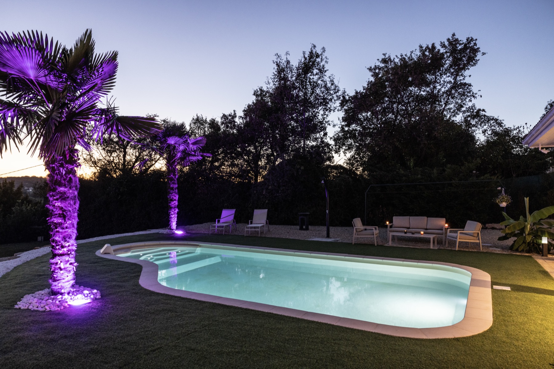 Beleuchteter Gartenpool am Abend mit Palmen und Lounge-Bereich